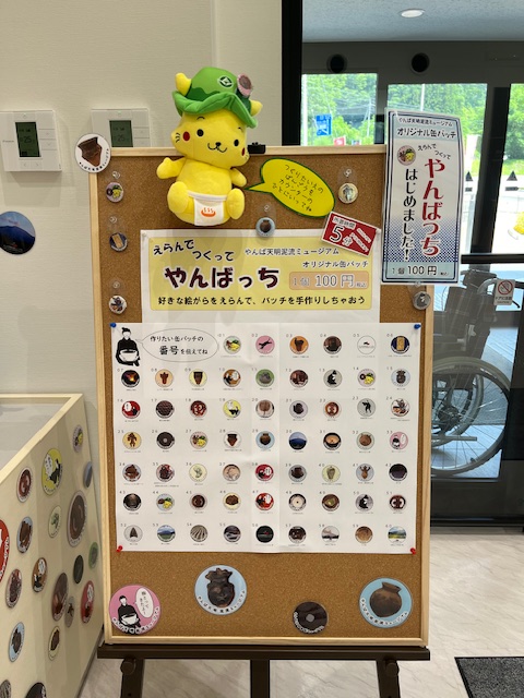 オリジナル図柄の缶バッチ「やんばっち」の看板